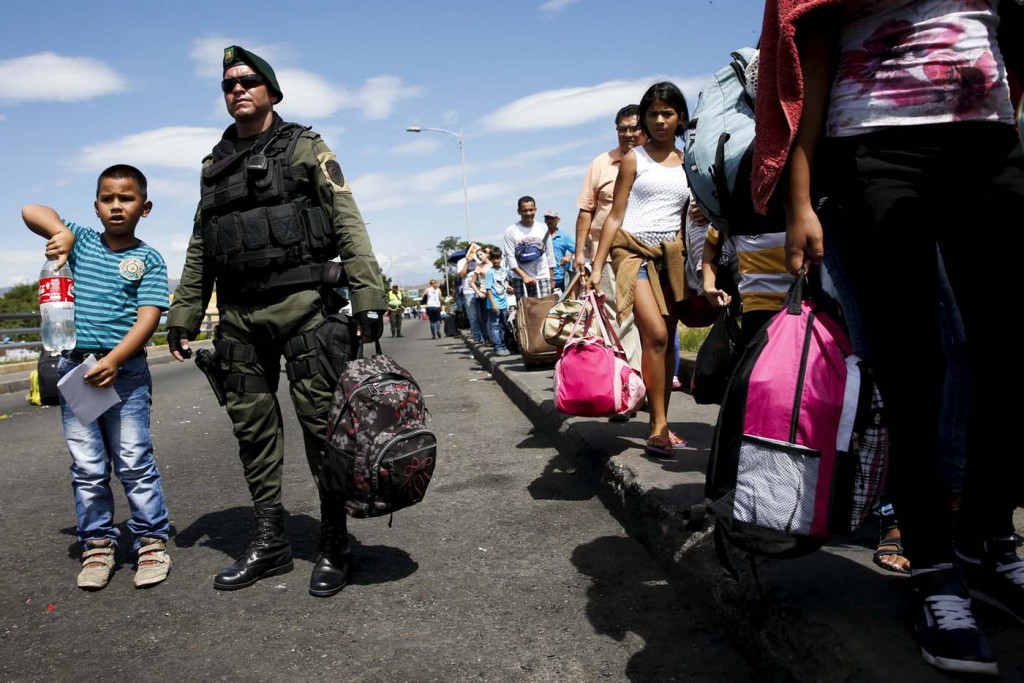 A child stands next to a Colombian policeman while they look for relatives as he crosses the Simon Bolivar bridge on the border with Colombia at San Antonio in Tachira state, Venezuela, August 26, 2015. Hundreds of Colombians waded across a border river with fridges, chickens and mattresses on their backs as goats and children followed under the scorching tropical sun, victims of an escalating dispute with Venezuela's government. Saying they were forced from their rickety wooden or corrugated metal homes and scared of what might happen next if they stayed inside Venezuela, they fled across the River Tachira and back into their homeland on Tuesday. REUTERS/Carlos Garcia Rawlins