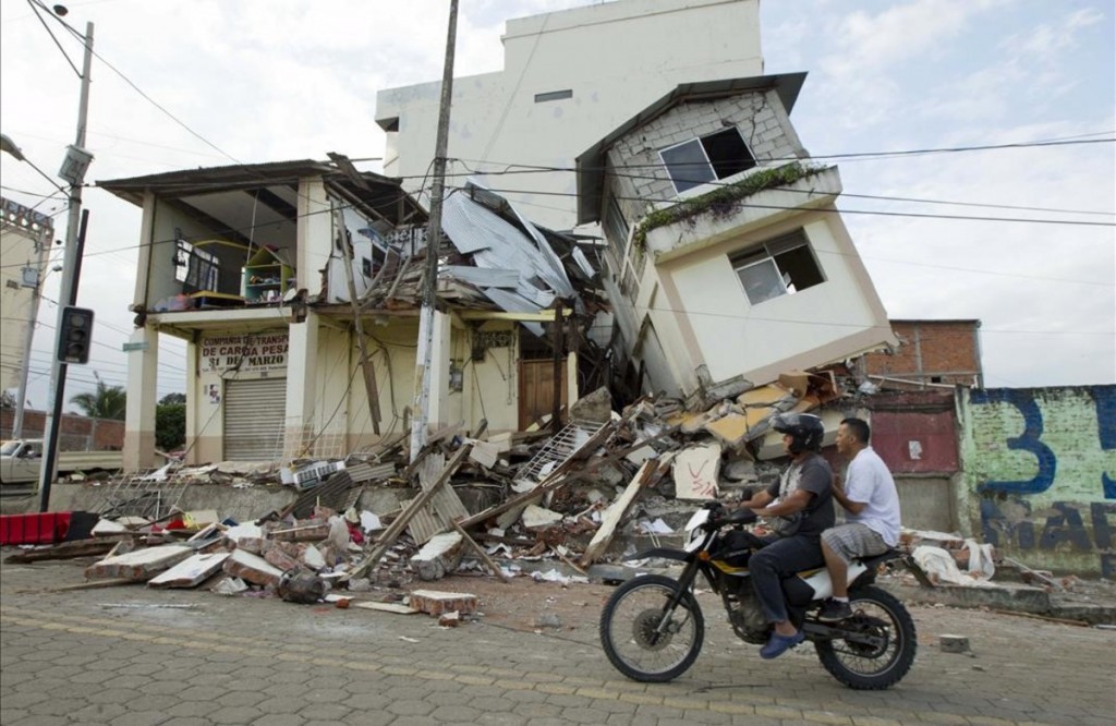 Men ride a motorcycle past damaged buildings in Pedernales