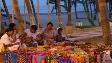 Indígenas wayúu tejiendo mochilas en el camellón de Riohacha. &nbsp; &nbsp; Riohacha, capital de La Guajira, presenta una realidad compleja con desafíos sociales (pobreza, informalidad, migración), económicos (dependencia del sector [&hellip;]