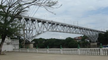 Impresionante toma lateral del Puente Férreo de Girardot-Flandes, una compleja estructura metálica de celosía que se alza en arco sobre la vegetación, vista desde la plazoleta del mirador.  