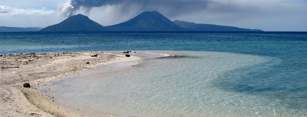 Una paradisíaca playa de arenas claras y aguas cristalinas contrasta con la imponente fuerza de la naturaleza al fondo. Allí, un volcán en plena erupción alza una densa y oscura [&hellip;]