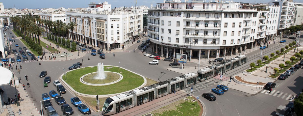 Una vista aérea de Rabat  muestra la  concurrida  Avenida Mohamed V, con una fuente central de agua en el medio. Un tranvía circula junto a la rotonda y muchos vehículos [&hellip;]